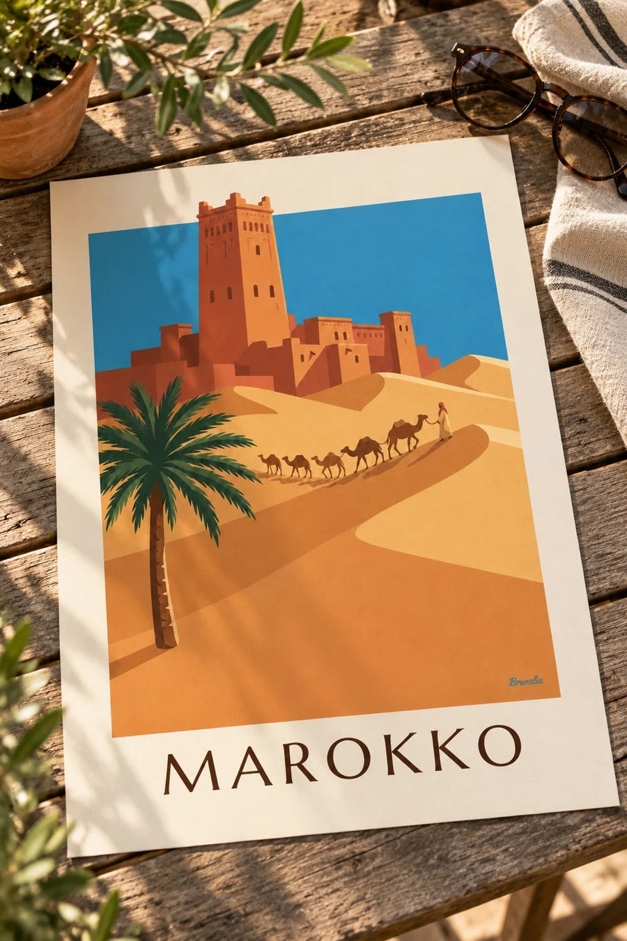 Plakat med kasbah og kamelkaravane i den marokkanske ørken: placeret på et bord