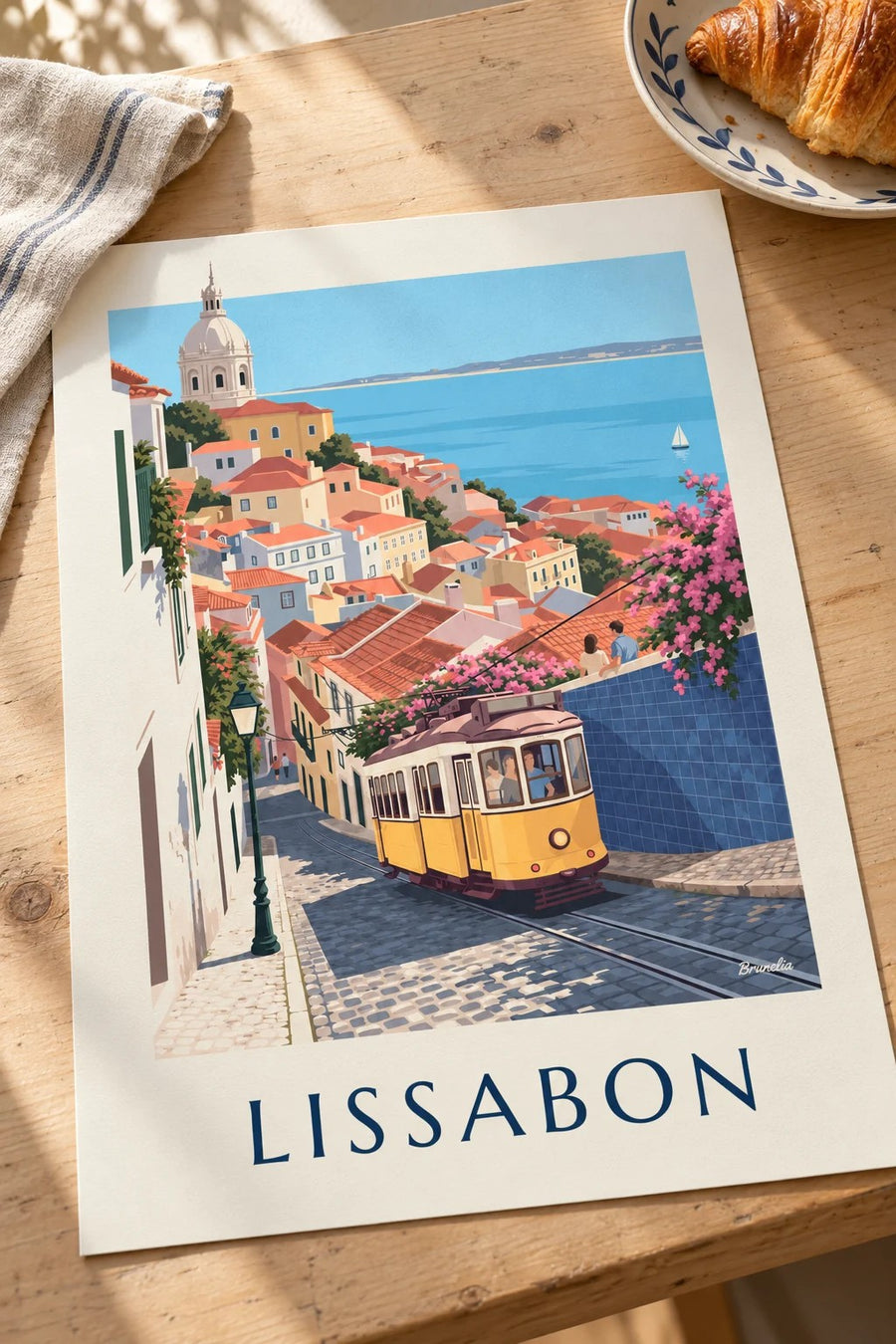 Plakat med gul sporvogn på brostensbelagt gade i Lissabon med udsigt til Tejo: lagt fladt på et bord
