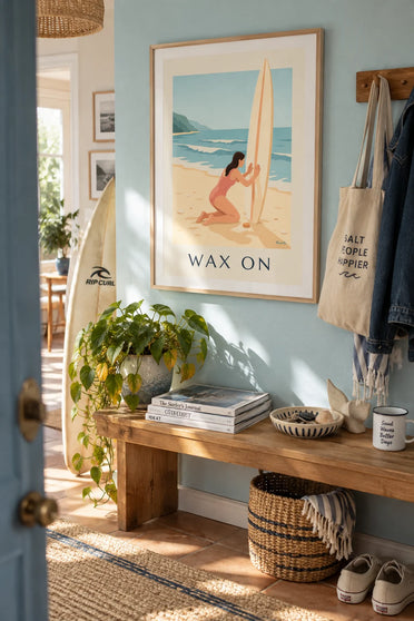 Poster of a female surfer waxing her board on the beach before the session: framed on the wall